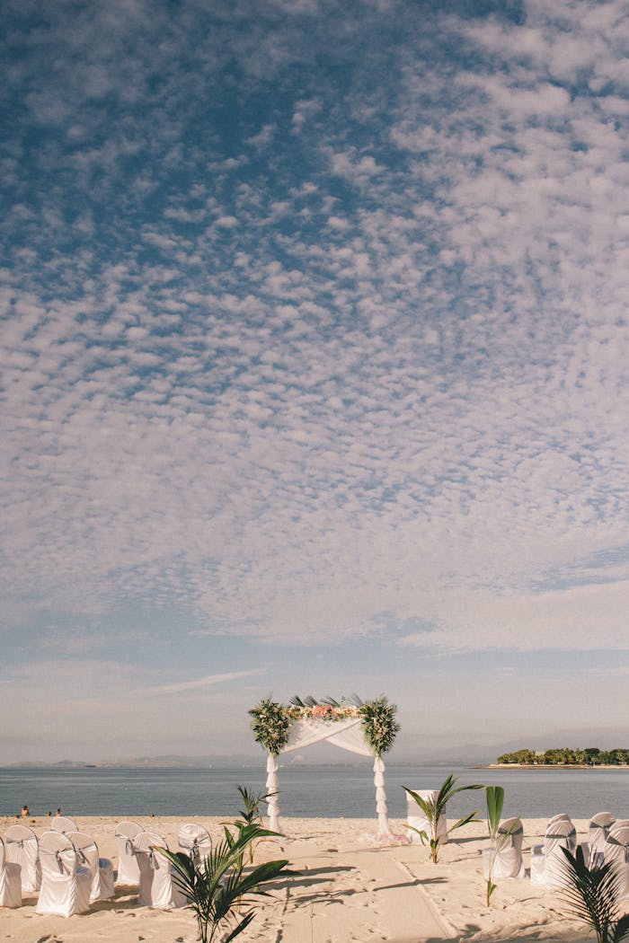 Scenic beach wedding setup with a floral arch and white chairs, perfect for tropical celebrations in Fiji.